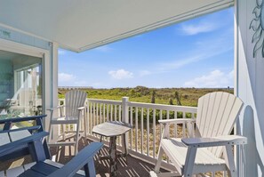 Ein Balkon mit Adirondack-Stühlen und einem Tisch, der auf eine grüne Landschaft und ein entferntes Gebäude blickt.