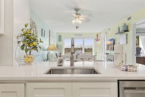 Una cocina con mostrador blanco, pileta de acero inoxidable y ventilador de techo.