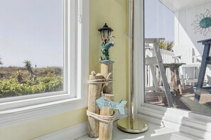 Ein Holzboden mit Laterne und einem Schild mit der Aufschrift 'BEACH', ein weißer Stuhl und ein weißer Zaun vor einem Fenster.