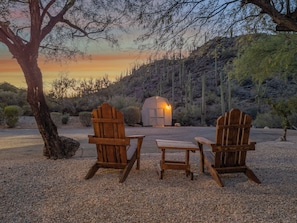 Two wooden Adirondack chairs, a small wooden table, and a rustic wooden structure with a light source. - Saguaro's Neighbor | Private Pool & Desert Views (Tucson)
