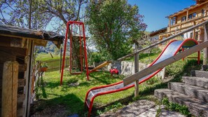 Ein Spielplatz mit Rutschen und Schaukeln, umgeben von einem Holzzaun und Bäumen.