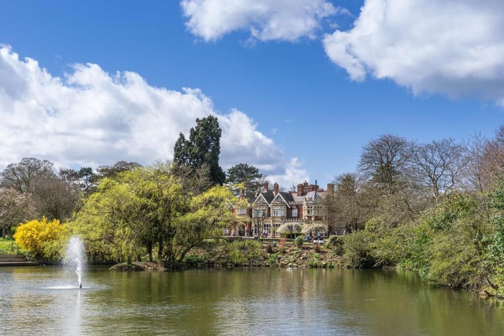 A historic building with a pond and fountain, surrounded by trees and a clear sky.