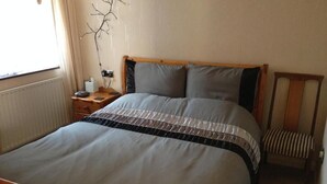 Een bed met houten frame, een nachtkastje met lamp en een stoel met gestreept kussen.