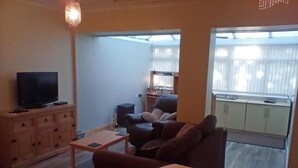 Een woonkamer met een televisie, bank, salontafel en uitzicht op een balkon met een raam.