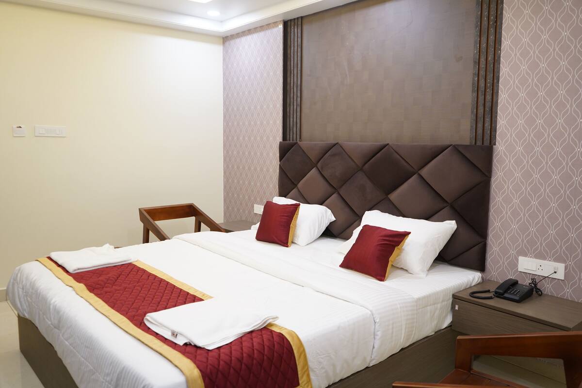 Una habitación de hotel con una cama grande, una mesita de noche de madera, un teléfono y una silla.