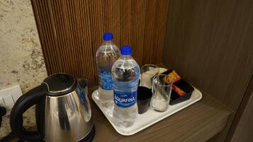 Una bandeja con una tetera, dos botellas de agua, un vaso y un pequeño recipiente.