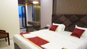 A hotel room with a large bed, a desk, and a chair. - JST Mahal and Residency (Tiruvannamalai)