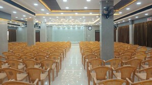 A conference room with rows of wicker chairs, a ceiling fan, and recessed lighting. - JST Mahal and Residency (Tiruvannamalai)