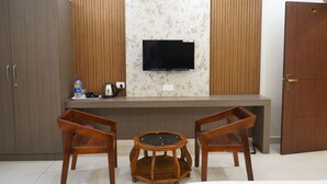 A room with a TV mounted on a wall, wooden furniture, and a cabinet. - JST Mahal and Residency (Tiruvannamalai)