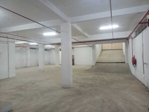 A spacious indoor area with concrete floors, white walls, and red pipes. - JST Mahal and Residency (Tiruvannamalai)