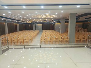 A spacious hall with rows of plastic chairs, a tiled floor, and a decorative ceiling design. - JST Mahal and Residency (Tiruvannamalai)