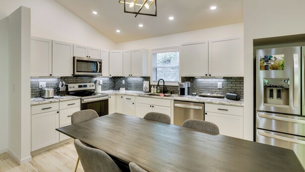 A modern kitchen with white cabinets, a dining table, and stainless steel appliances. - Sleek Hillside Getaway in Brevard, Dogs Welcome! (Brevard)