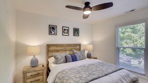A bedroom with a wooden headboard, a bed with floral bedding, two bedside tables with lamps, and a ceiling fan. - Sleek Hillside Getaway in Brevard, Dogs Welcome! (Brevard)