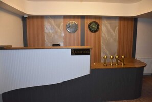 A reception desk with a 'RECEPTION' sign, two clocks, and three golden lamps. - Görele Liva Hotel (Görele)