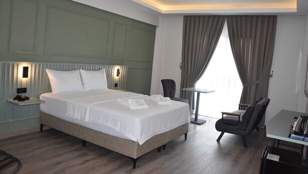Una habitación de hotel con una cama grande, mesitas de noche, un escritorio, una silla y una ventana con cortinas.
