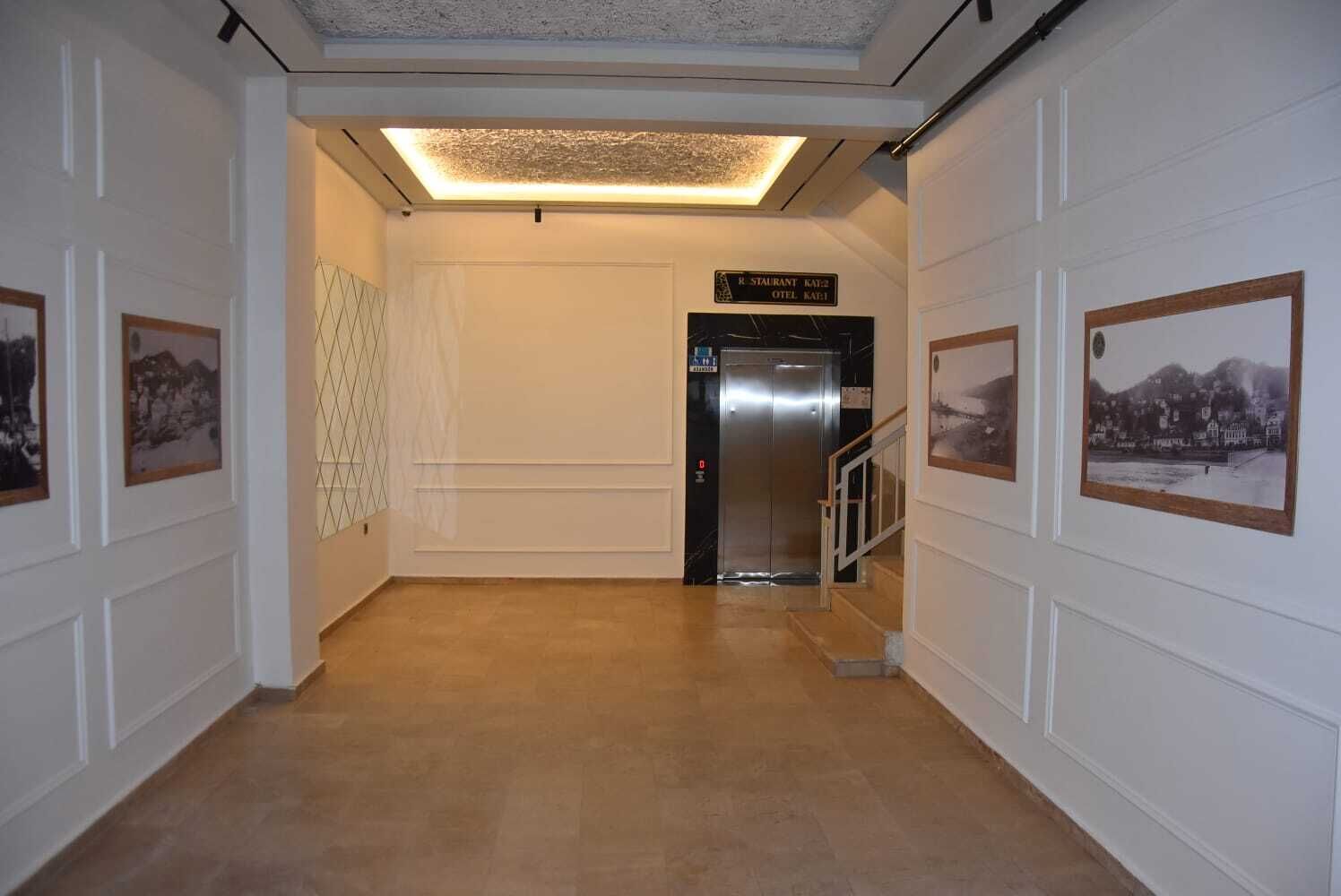A hallway with a modern elevator, framed pictures on the walls, and a tiled floor.