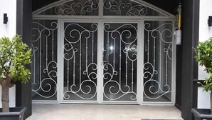 Entrada de restaurante con un letrero negro, puertas metálicas decorativas y plantas en macetas.
