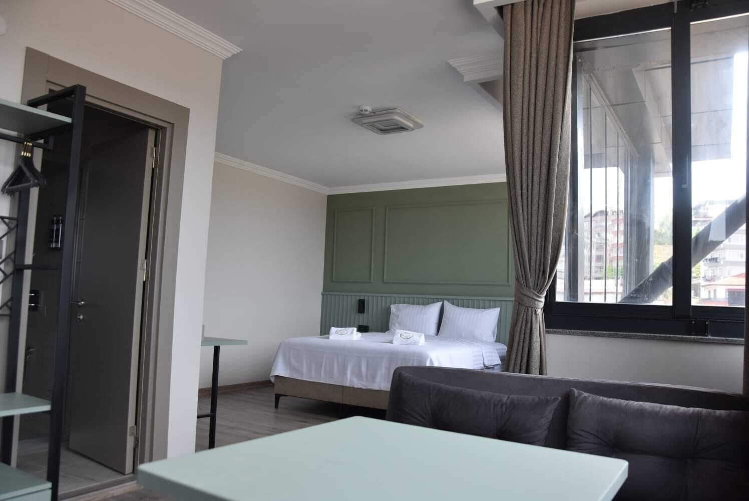 Quarto de hotel com cama, uma mesinha, um sofá e uma janela com cortinas.