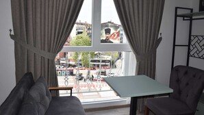 Una habitación con un ventanal grande, cortinas grises, un sofá, una silla y una mesa.