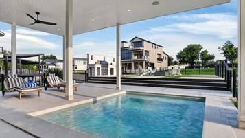 A swimming pool with lounge chairs, a ceiling fan, and a view of modern houses.