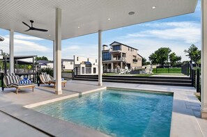 Une piscine dotée de chaises longues, d’un ventilateur de plafond et offrant une vue sur des maisons modernes.