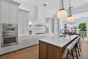 Une cuisine moderne avec des meubles blancs, des appareils en acier inoxydable et un grand îlot central doté de tabourets.