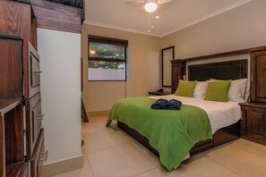 Un dormitorio con cama, ventana, ventilador de techo y muebles de madera.