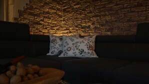 A cozy living area with a brick wall, a dark sofa, floral cushions, and a wooden side table with a bowl of nuts. - Apartment Sonnseite for max. 5 persons with sun terrace (Teisendorf)