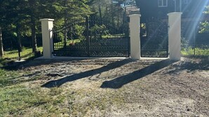Een hekpoort met een metalen poort, een gebouw met meerdere ramen, en een heldere lucht.