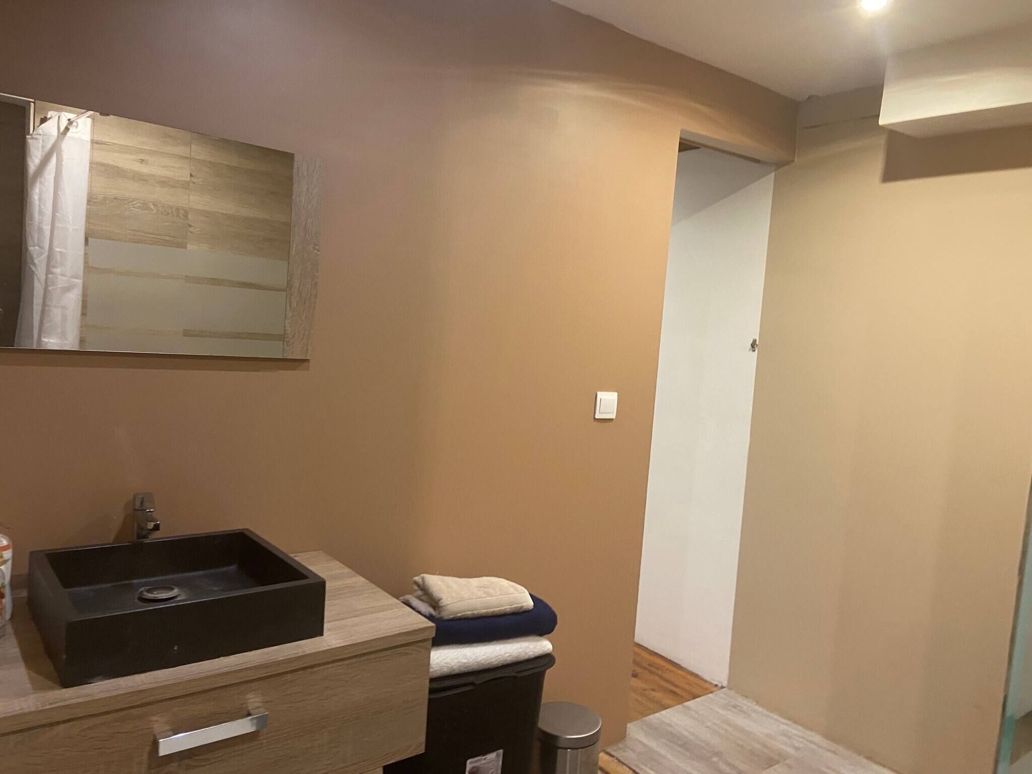 Un baño con tocador de madera, lavamanos negro, espejo y una toalla en el suelo.