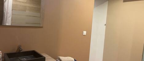 Un baño con tocador de madera, lavamanos negro, espejo y una toalla en el suelo.
