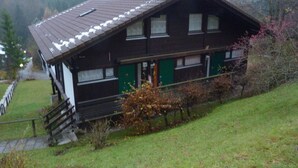 A two-story wooden house with a sloped roof, a front porch, and a visible staircase leading to the entrance. - Vacation apartment Lärch 17c (Siegsdorf)