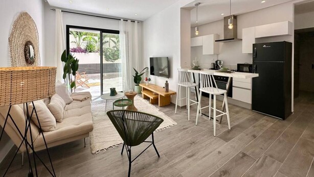 En moderne lejlighed med opholdstue, spiseplads, køkken og en balkon med planter.