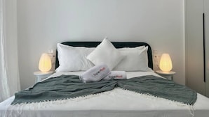 En seng med hvide sengetøj, et grønt pled og to puder, hvoraf den ene har teksten 'SuperHost'.