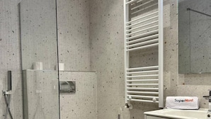 Et moderne badeværelse med en glasbrusekabine, toilet, vask med håndklæder og spejl.