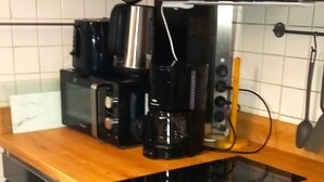 A kitchen with a black stove, a coffee maker, and a microwave on the counter. - Vacation apartment Glock 6 (Siegsdorf)