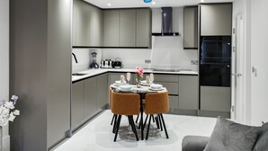 A modern kitchen with grey cabinets, a dining table with two chairs, and a refrigerator. - Apartment 2 - UK51647 (Maldon)