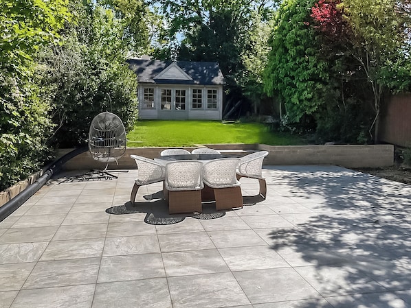 Une terrasse avec une table et des chaises, une cage à oiseaux et une maison en arrière-plan.