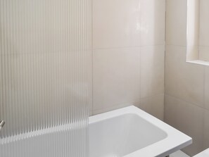 Ein Badezimmer mit einer weißen Badewanne, einem vertikalen Lüftungsgitter und gefliesten Wänden.