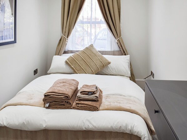 A neatly made bed with folded towels, a pillow, and a window with curtains.