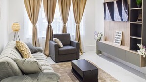 A living room with a sofa, armchair, coffee table, and a TV on a shelf. - Apartment 2 - UK51647 (Maldon)