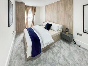 A modern bedroom with a bed, nightstand, and wall-mounted lamp.