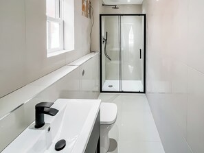 Une salle de bain moderne avec un lavabo blanc, des toilettes et une douche à parois de verre.