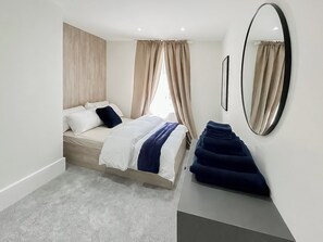 Ein modernes Schlafzimmer mit Bett, Vorhängen, einem Spiegel und einem ordentlich bezogenen Bett.