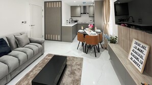 Un soggiorno moderno con divano, tavolo da pranzo per sei persone, cucina sullo sfondo e TV a parete.