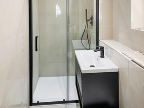 Ein modernes Badezimmer mit einer Glaskabine zur Dusche, einem weißen Waschbecken und einem schwarzen Schrank.