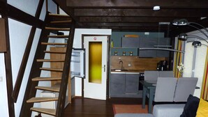 A modern kitchen with a built-in stove, a dining area with a gray sofa and a small table, and a wooden staircase leading to another level.
