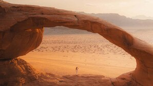 A natural rock arch formation with a person standing in the center. - Magic rum hussen Luxury (Wadi Rum Village)