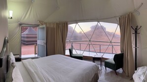 Une pièce aménagée avec une tente, un lit, une chaise, un porte-manteau et une vue sur un paysage désertique.