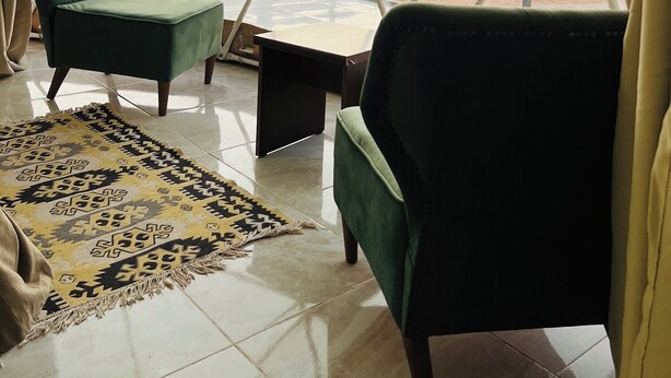 Une pièce avec vue sur les montagnes, une chaise verte, une petite table et un tapis à motifs.